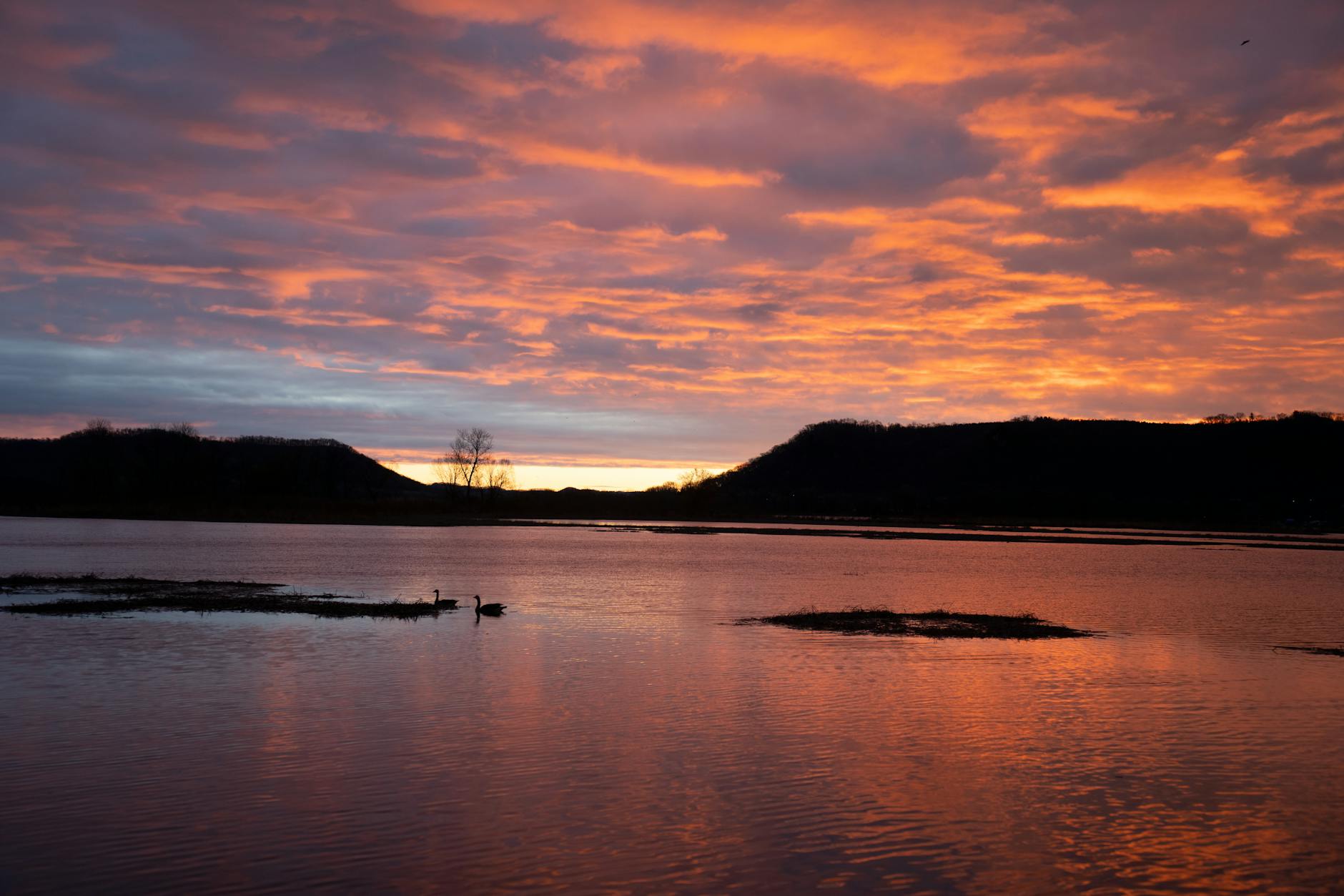 Kolorowy zachód słońca nad spokojną rzeką i wzgórzami pod Wadowicami