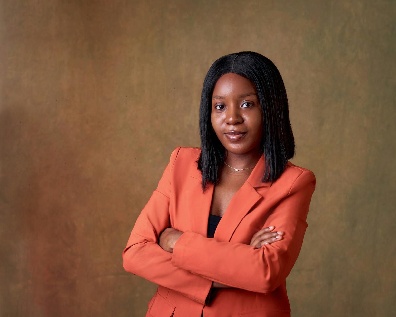 Pewna siebie kobieta w pomarańczowej marynarce pozuje z założonymi rękami